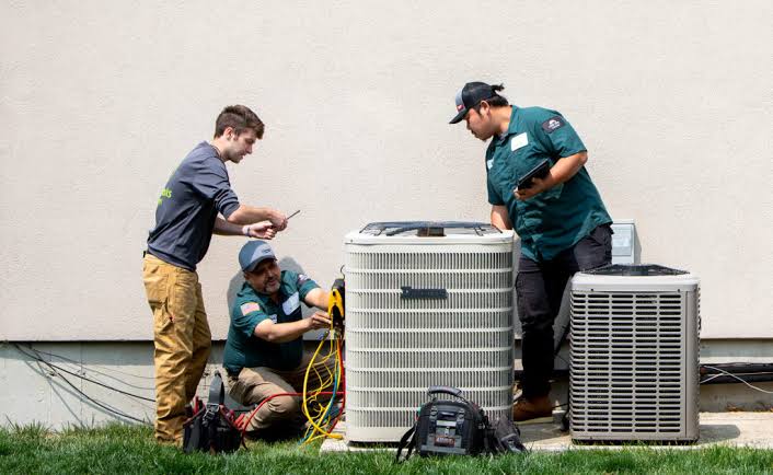 Three HVAC technicians working together on residential cooling equipment